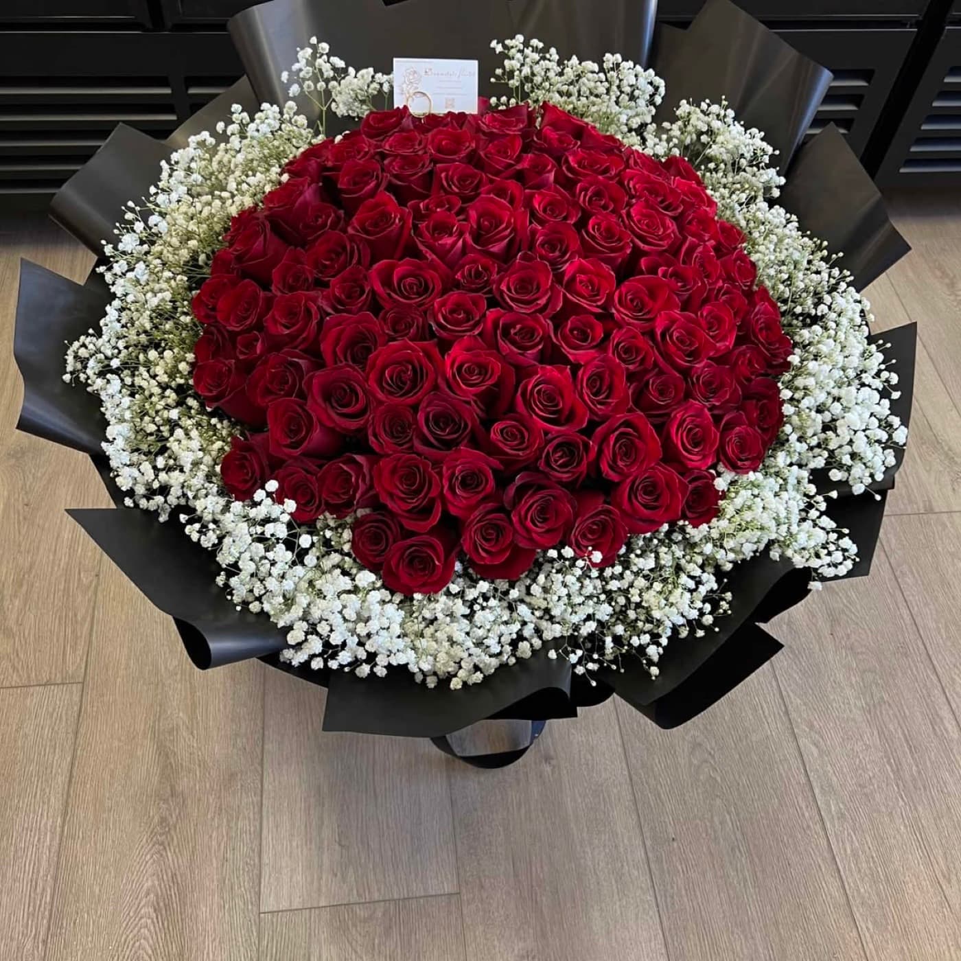A hundred red roses in a ring of baby's breath, wrapped in black